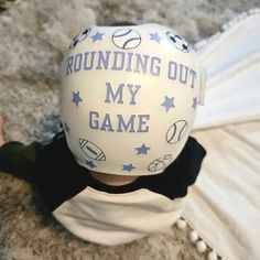 a young child wearing a white helmet with blue stars and the words rounding out my game on it