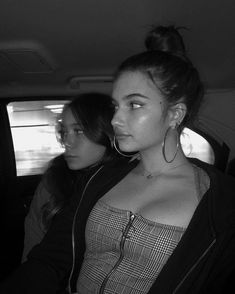 two women sitting in the back seat of a car, one with large hoop earrings