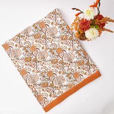 an orange and white floral print napkin next to a vase with flowers