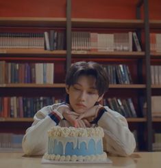 a young boy sitting at a table with a cake in front of him and bookshelves behind him