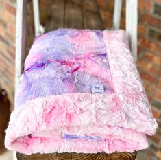 a pink and purple blanket sitting on top of a wooden chair next to a brick wall