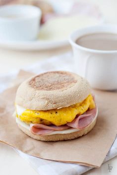 a sandwich with ham, egg and cheese on it next to a cup of coffee