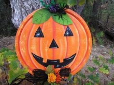 an orange pumpkin decorated with black and green leaves sits in front of a large tree