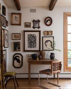 there are many framed pictures on the wall and a table with a chair in front of it