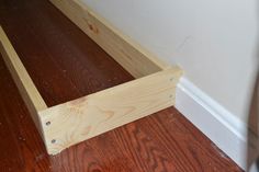 an unfinished piece of wood sitting on top of a hard wood floor next to a wall