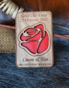 a wooden save the date magnet with a rose in it on top of a pile of other items