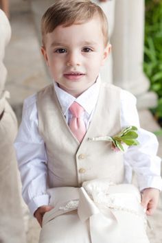 a little boy dressed in a suit and tie with a flower on his lapel