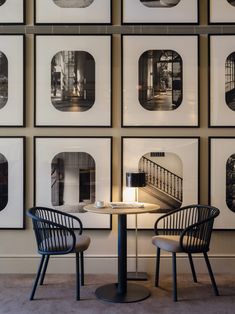 two chairs sitting at a table in front of pictures on the wall behind them and a lamp next to it