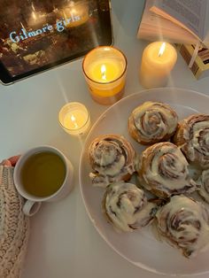 a white plate topped with pastries next to a cup of tea and candlelight