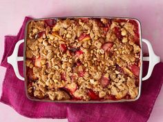 a casserole dish filled with fruit and crumbled toppings on a purple cloth