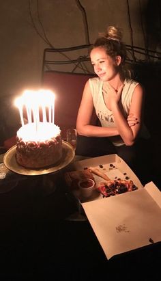 a woman sitting in front of a cake with lit candles