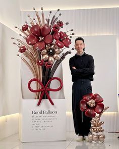 a man standing next to a vase with red flowers in it and a bow on top