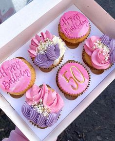 four cupcakes with pink and purple frosting are in a box that says happy birthday