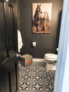 a bathroom with black and white tile flooring and a painting on the wall above the toilet