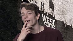 a man standing in front of a brick wall holding his finger to his mouth and looking at the camera