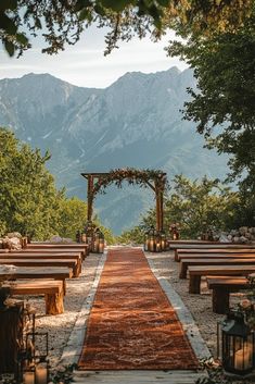 an outdoor ceremony setup with wooden benches and greenery on the ground in front of mountains