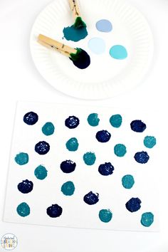 a paper plate with some paint on it next to a painting brush and blue circles