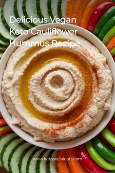 Cauliflower hummus drizzled with olive oil and paprika, surrounded by colorful sliced vegetables.