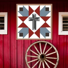 an old wagon wheel is in front of a red barn with a cross on it