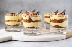 four desserts in small glass cups on a white board with chocolate shavings