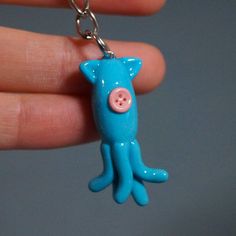 a small blue toy with a pink button on it's face is being held by a hand