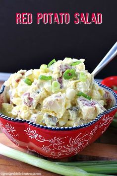 a red bowl filled with potato salad on top of a wooden table next to celery