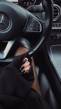 a woman with black nails is sitting in the driver's seat of a car