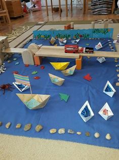 paper boats are on the ground in front of a blue tablecloth with rocks and stones