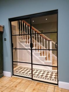 an open glass door leading to a stair case in a room with hardwood floors and blue walls