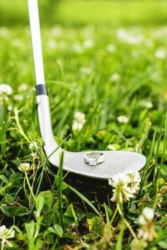 a golf club sitting in the grass next to a hole with a wedding ring on it