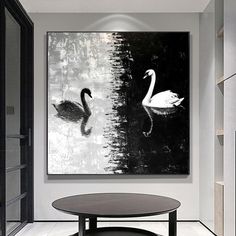 a black and white painting with swans in the water next to a round coffee table