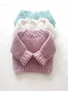 three knitted sweaters sitting next to each other on top of a white surface