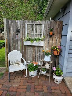 an old chair and some potted plants in front of a wooden fence on a brick patio