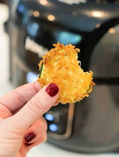 someone is holding up a fried food item in front of an air fryer