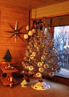 a small christmas tree sitting in front of a window next to a wooden table with ornaments on it