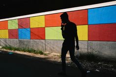 a man walking down the street while talking on his cell phone in front of a colorful wall