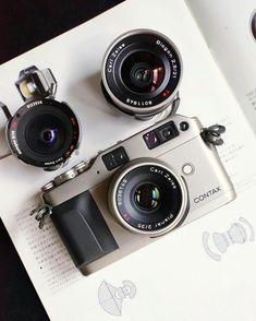 two cameras sitting on top of an open book with the same lens attached to it