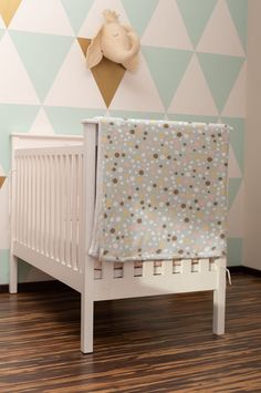 a baby crib in front of a wall with geometric designs on it and a wooden floor