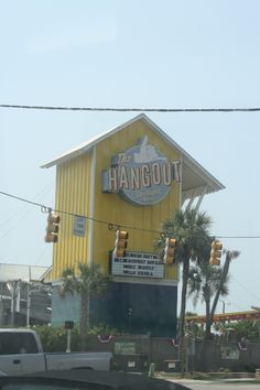 a yellow hangout sign on the side of a building with palm trees in front of it