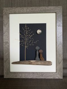 a wooden frame with rocks and a small tree in the middle on a wall next to a couch