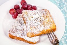 two pieces of french toast with powdered sugar on top and grapes in the background