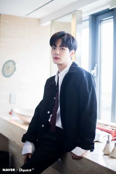 a young man wearing a suit and tie sitting on a counter next to a window