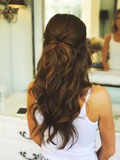 a woman with long brown hair standing in front of a bathroom mirror looking at her reflection