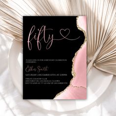 a black and pink party card with gold foil lettering on it, next to a fan