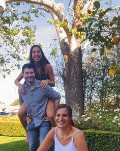 a man and woman sitting on top of each other in front of a tree