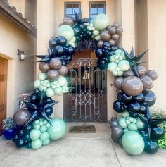 an arch made out of balloons in front of a house with a gate and entrance