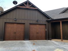 two brown garage doors are open in front of a large gray building with dark wood trim