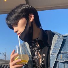 a young man drinking from a glass with a straw in his mouth while wearing a denim jacket