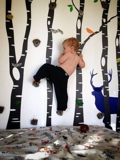 a young boy laying on top of a bed next to a forest mural