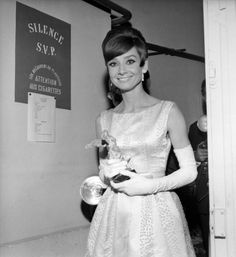 an old photo of a woman in a dress and gloves holding a glass award while standing next to a man